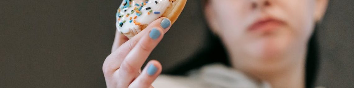 Crop emotionless female in casual wear chewing tasty doughnut glazed with vanilla icing in light room